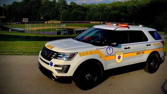An EMS quick-response SUV with red and white lights and a yellow stripe down the side. 